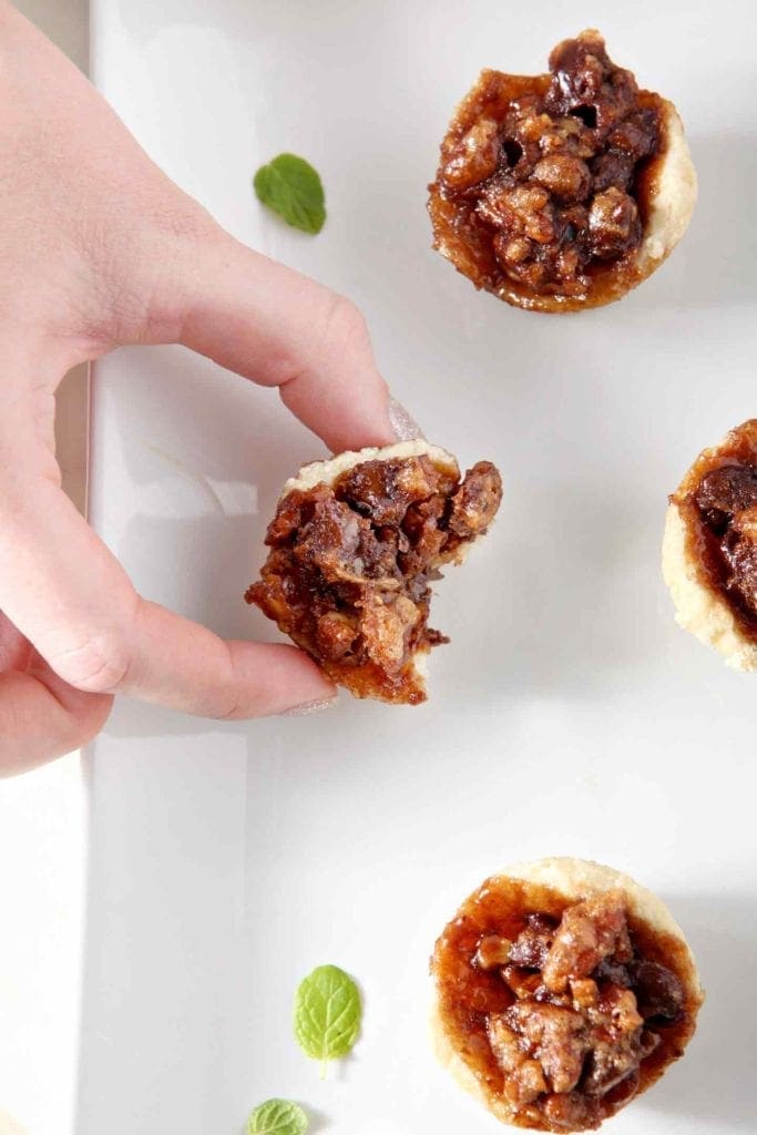 A Mini Bourbon Chocolate Pecan Pie is grabbed from a white platter before serving