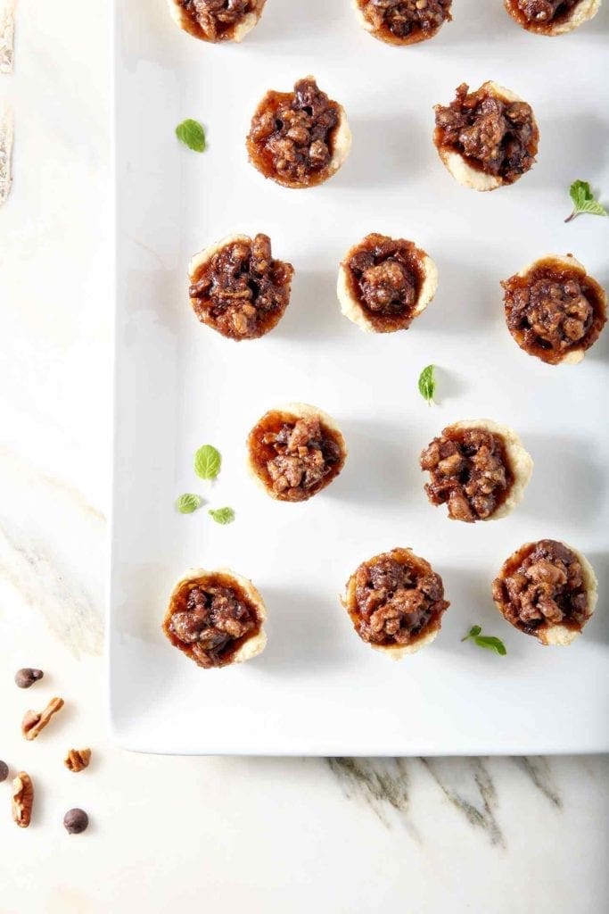 Mini Bourbon Chocolate Pecan Pies, after baking, on a white platter.