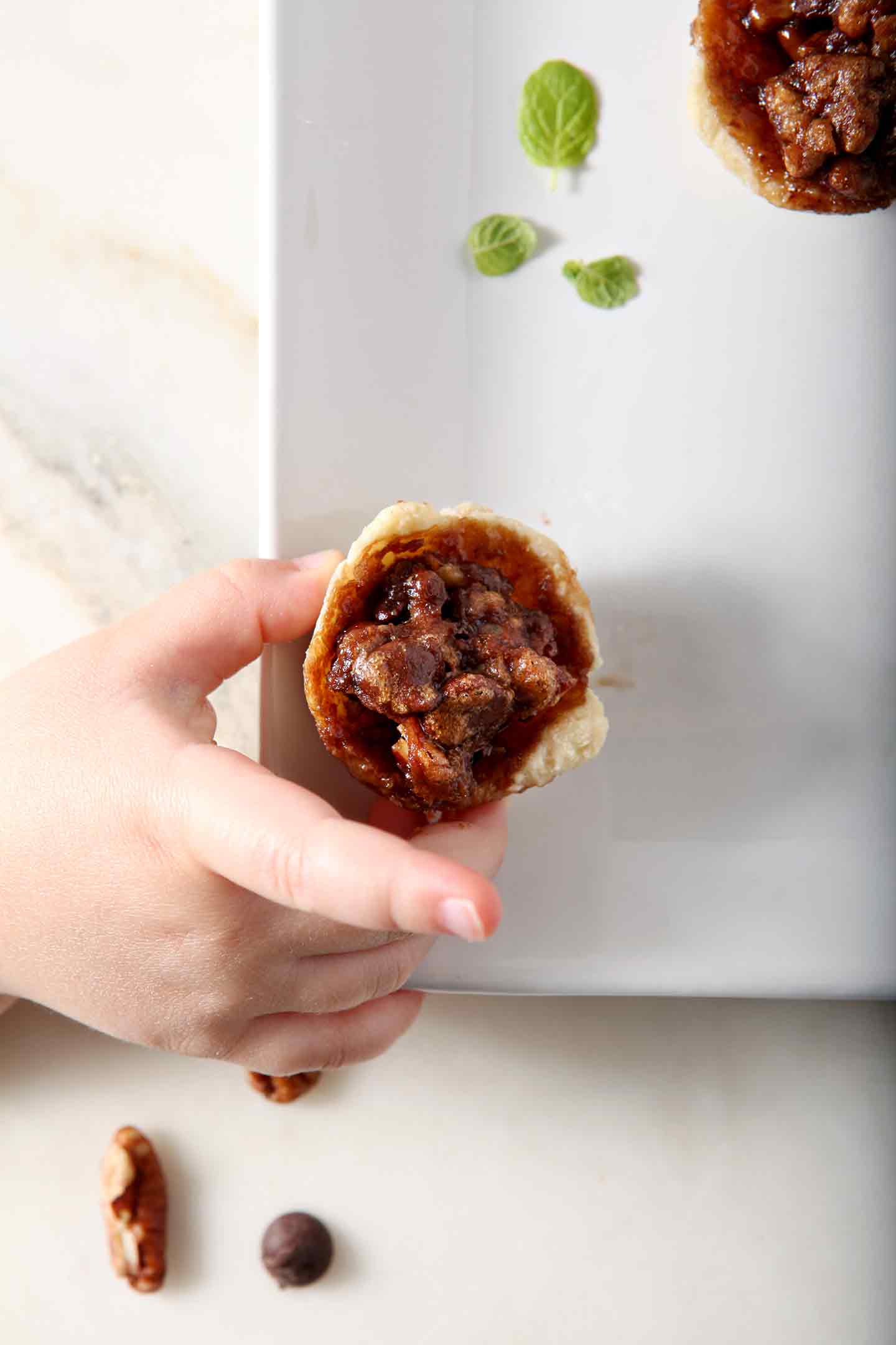 A Mini Bourbon Chocolate Pecan Pie is grabbed from a white platter before serving