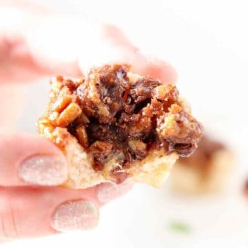 A bitten-into Mini Bourbon Chocolate Pecan Pie is held in hand before being enjoyed.