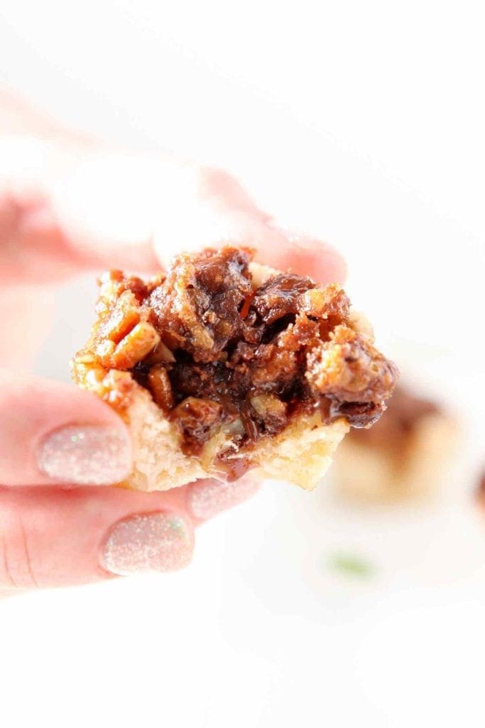 A bitten-into Mini Bourbon Chocolate Pecan Pie is held in hand before being enjoyed.