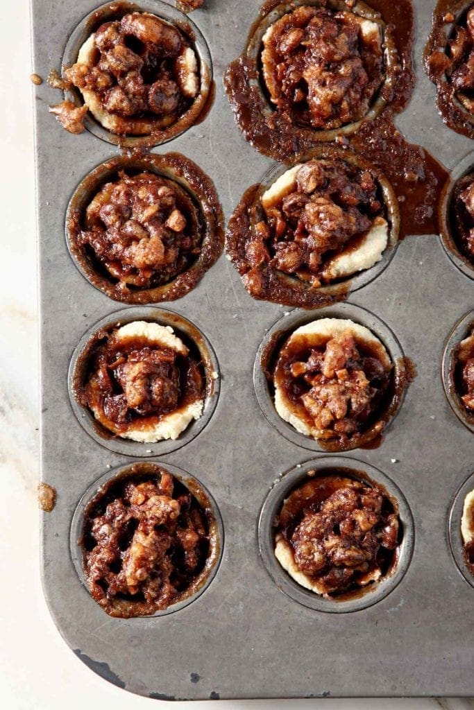 Mini Bourbon Chocolate Pecan Pies, still in the mini muffin tin, directly after baking on a marble background