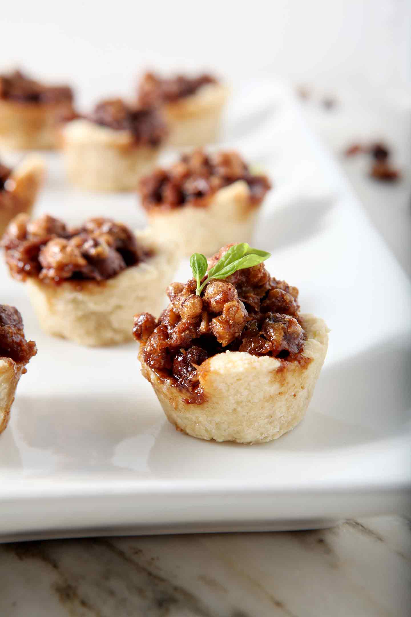 Mini Bourbon Chocolate Pecan Pies, after baking, on a white platter.