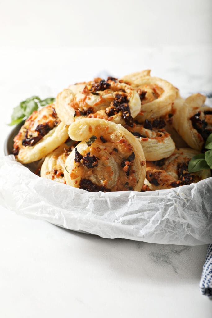 A bowl of puff pastry pinwheels with bruschetta flavors on marble