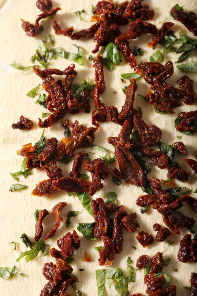 Sun-dried tomatoes on top of fresh basil and butter on rolled out puff pastry