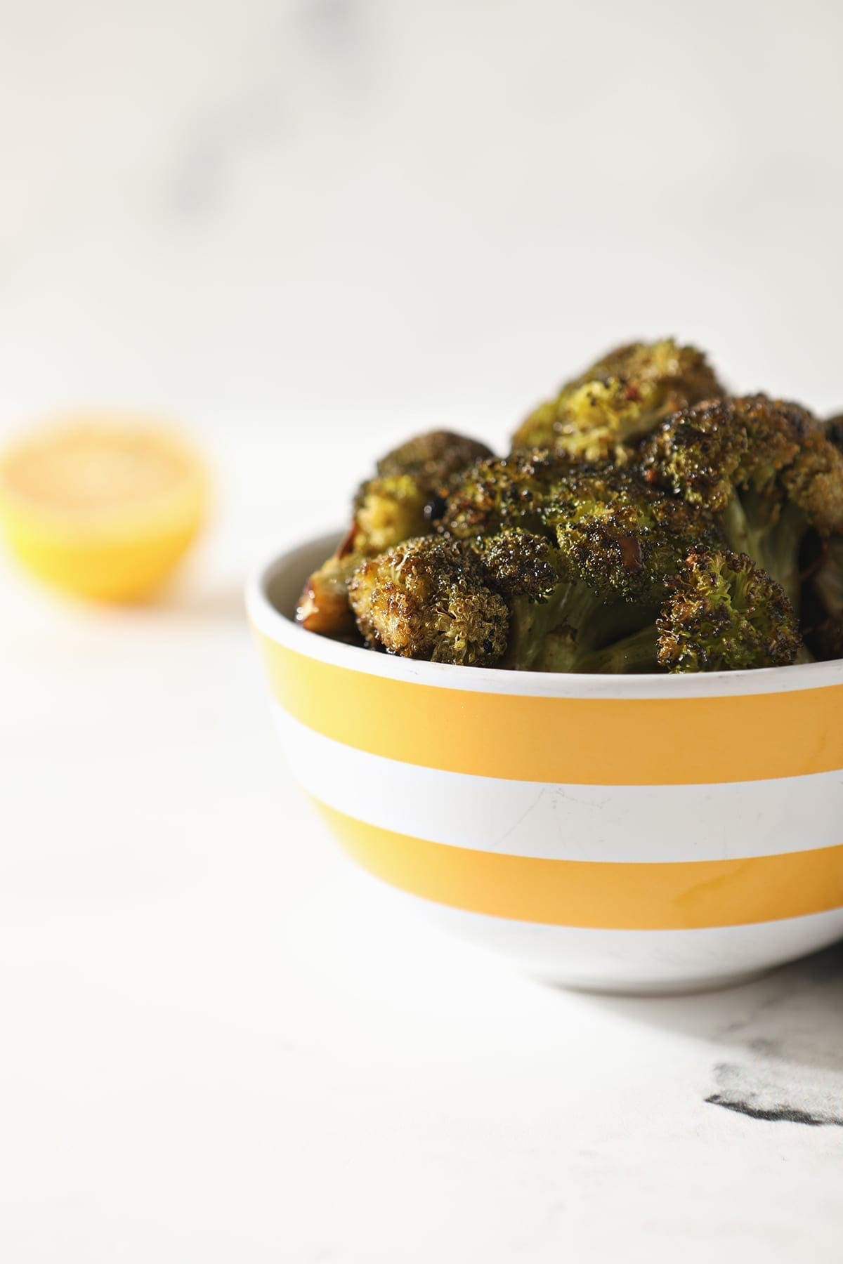 Roasted Broccoli with Lemon and Garlic in a yellow and white striped bowl sitting on a marble counter