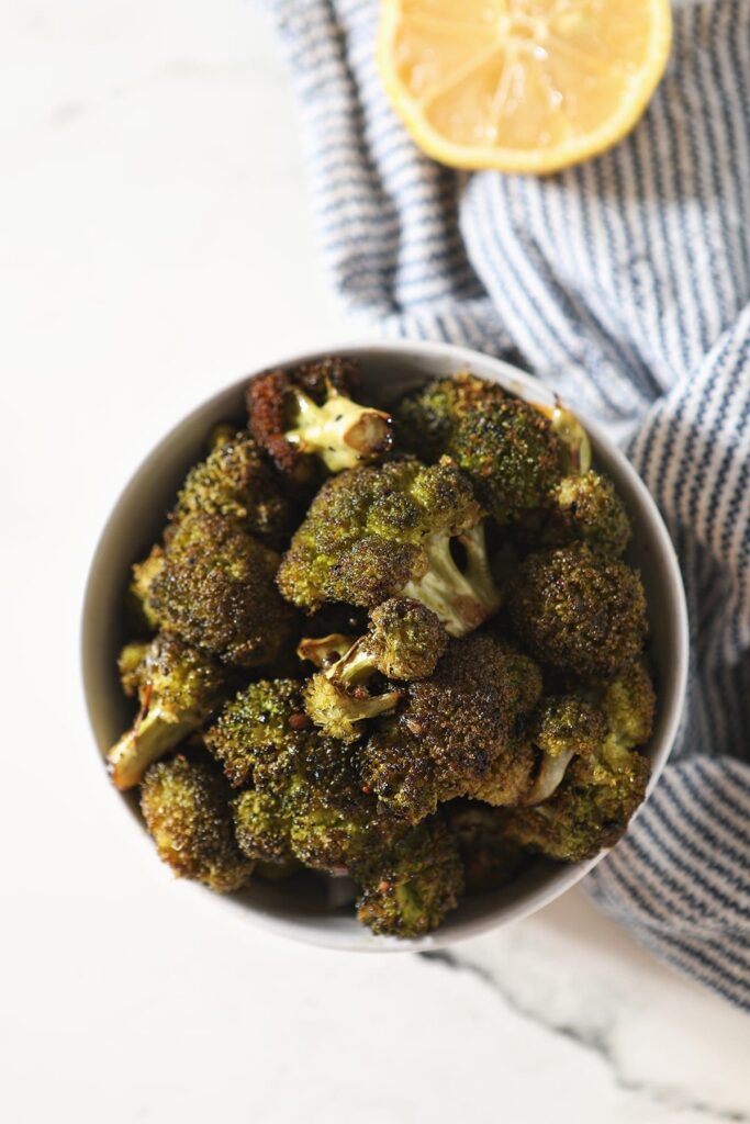 Roasted Broccoli with Lemon in a bowl sitting on top of a blue and white striped towel next to a lemon wedge