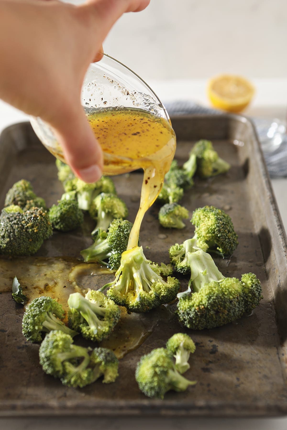 A vinaigrette pours over fresh broccoli on a sheet pan