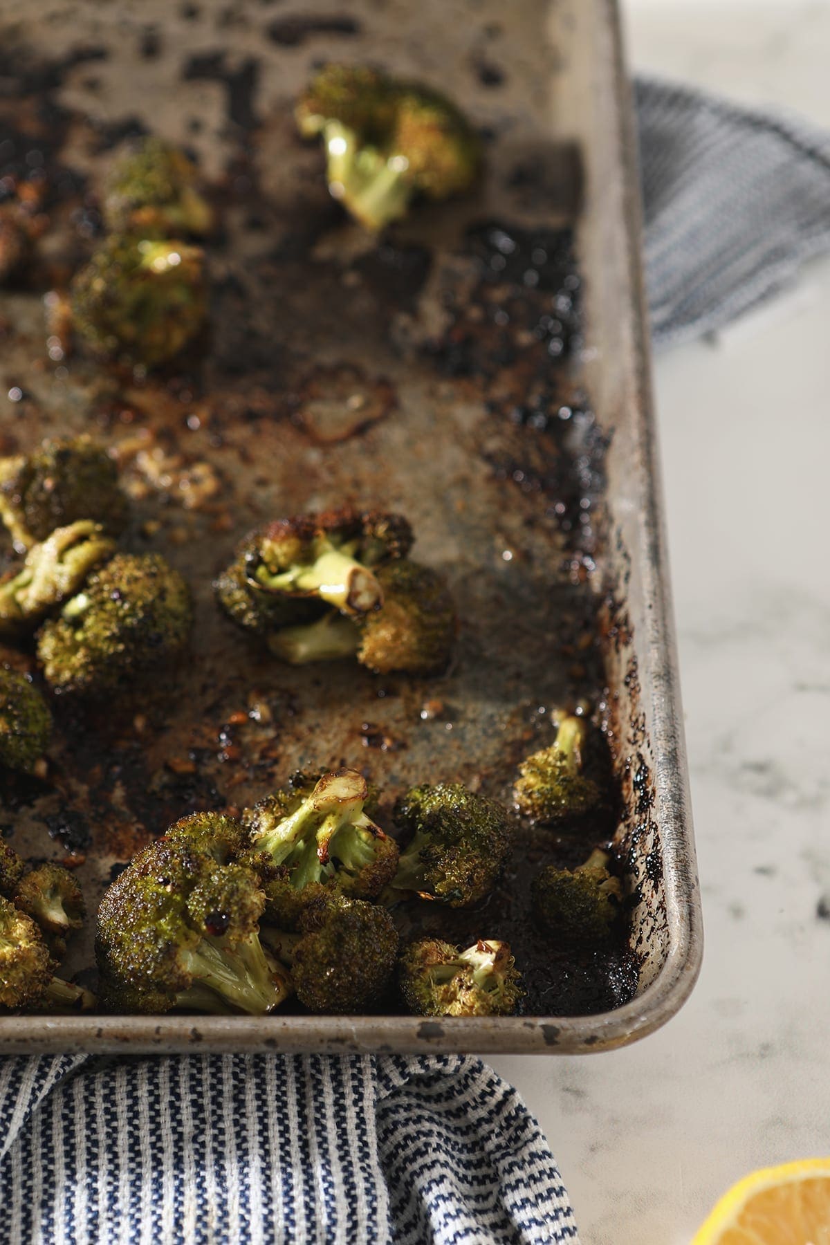 Roasted Broccoli with lemon and garlic on a sheet pan sitting on a blue striped towel after roasting