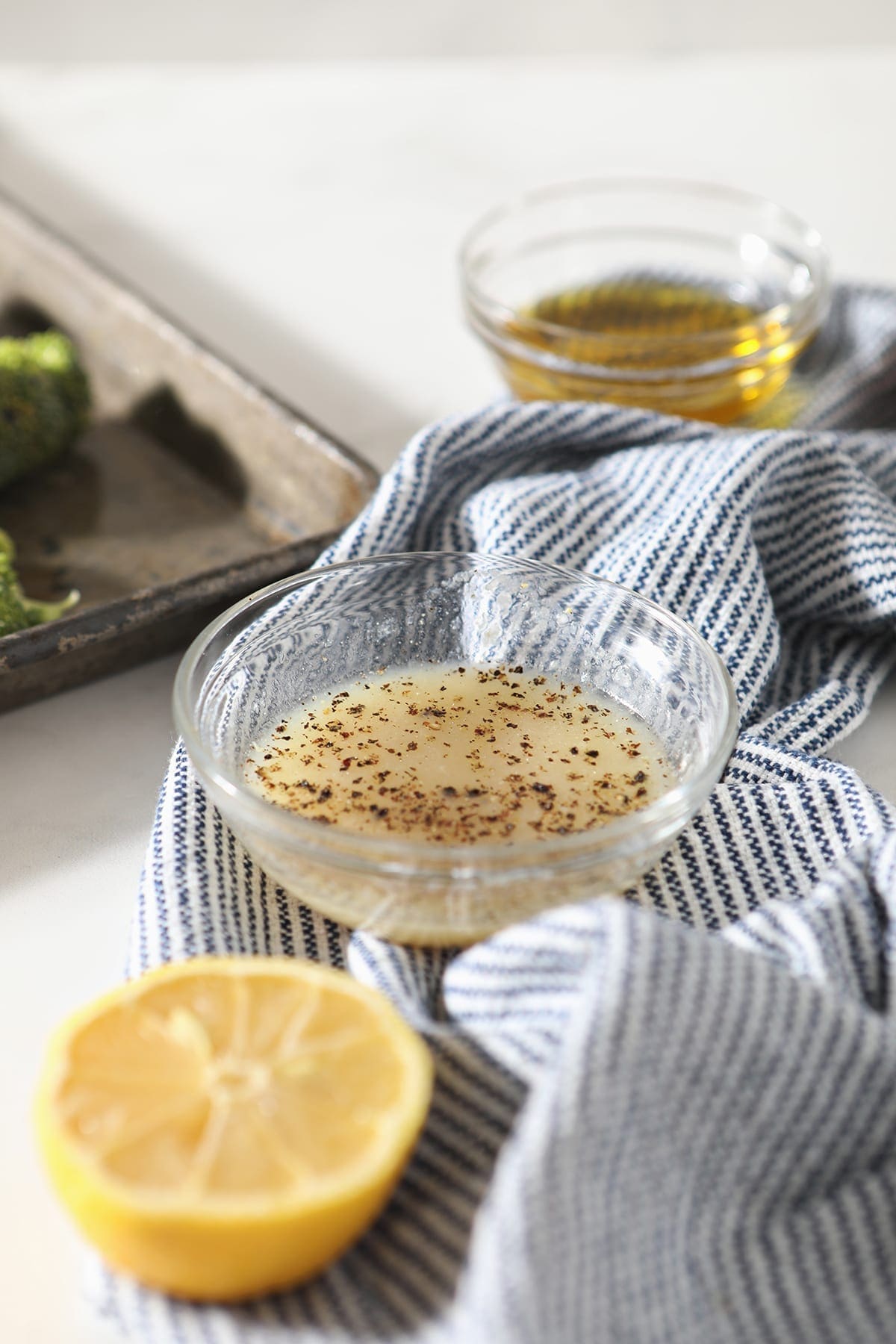 A vinaigrette in a glass bowl sits next to a lemon half and a bowl of oil