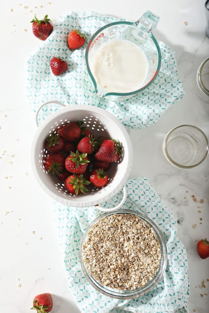 Fresh strawberries, oats and milk on a turquoise patterned towel next to mason jars