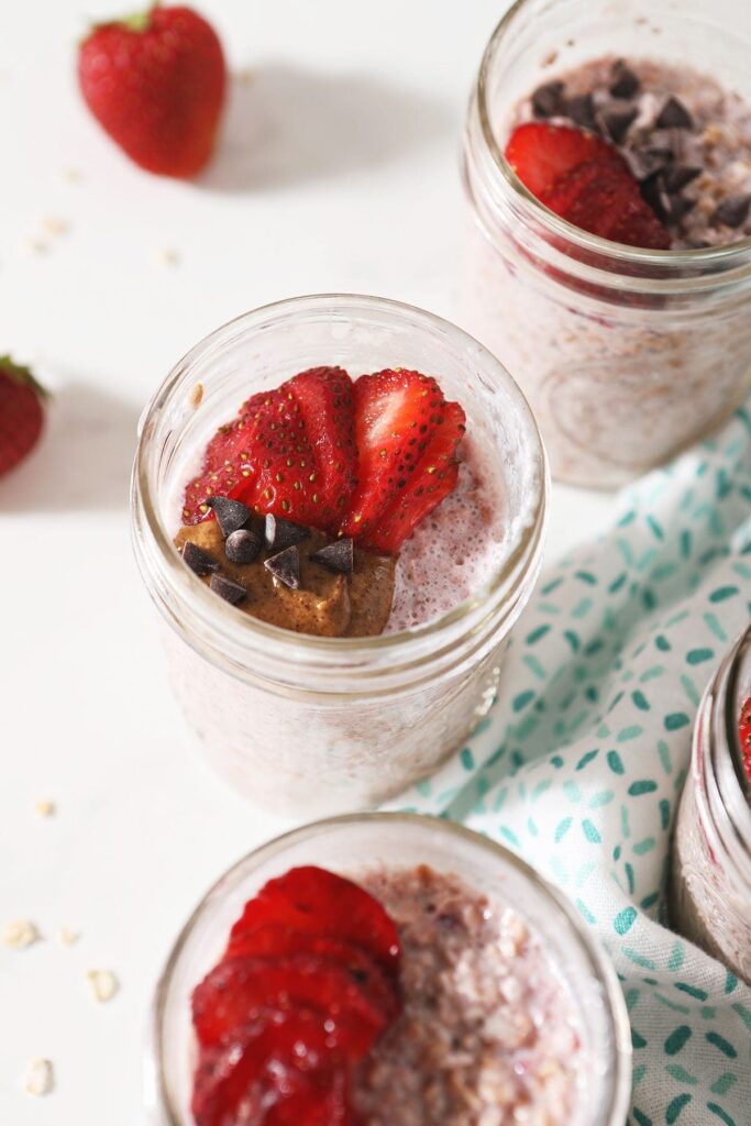 Close up of strawberry overnight oats in a mason jar garnished with almond butter, chocolate chips and sliced strawberries