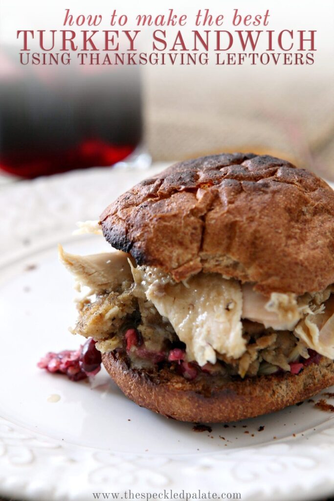 A sandwich with cranberry, turkey, stuffing and more on a white plate with the text 'how to make the best turkey sandwich using thanksgiving leftovers'