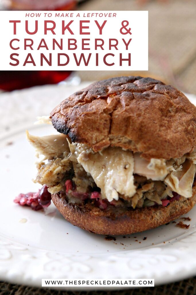 Close up of a sandwich with cranberry, turkey, stuffing and more on a white plate with the text 'how to make a leftover turkey & cranberry sandwich'