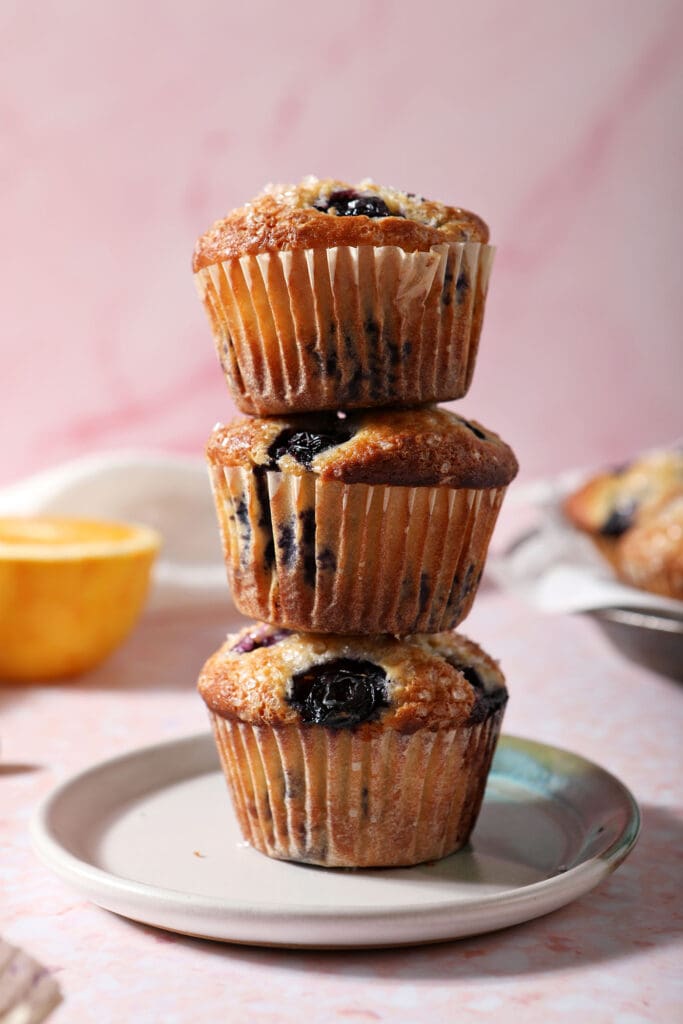 A plate holds three stacked blueberry muffins on top of each other in front of an orange