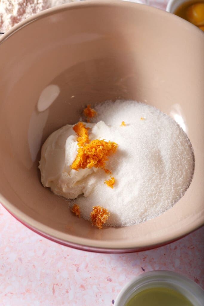 Sugar, orange zest and sour cream in a bowl on a pink surface