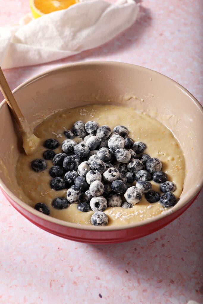 Blueberries coated in flour sit on top of muffin batter before mixing