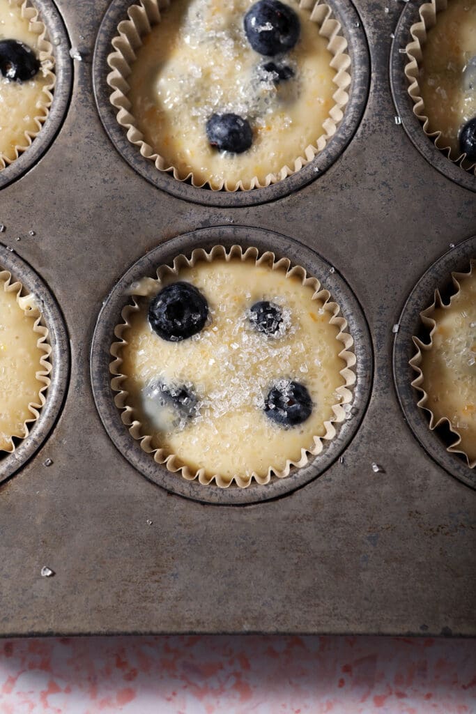 Sour Cream Blueberry Muffin batter in a muffin tin with sparkling sugar on top before baking