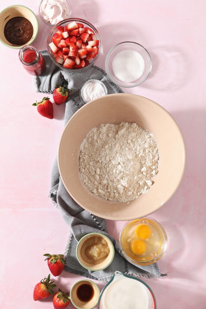 Ingredients to make pancakes with strawberries on a pink background