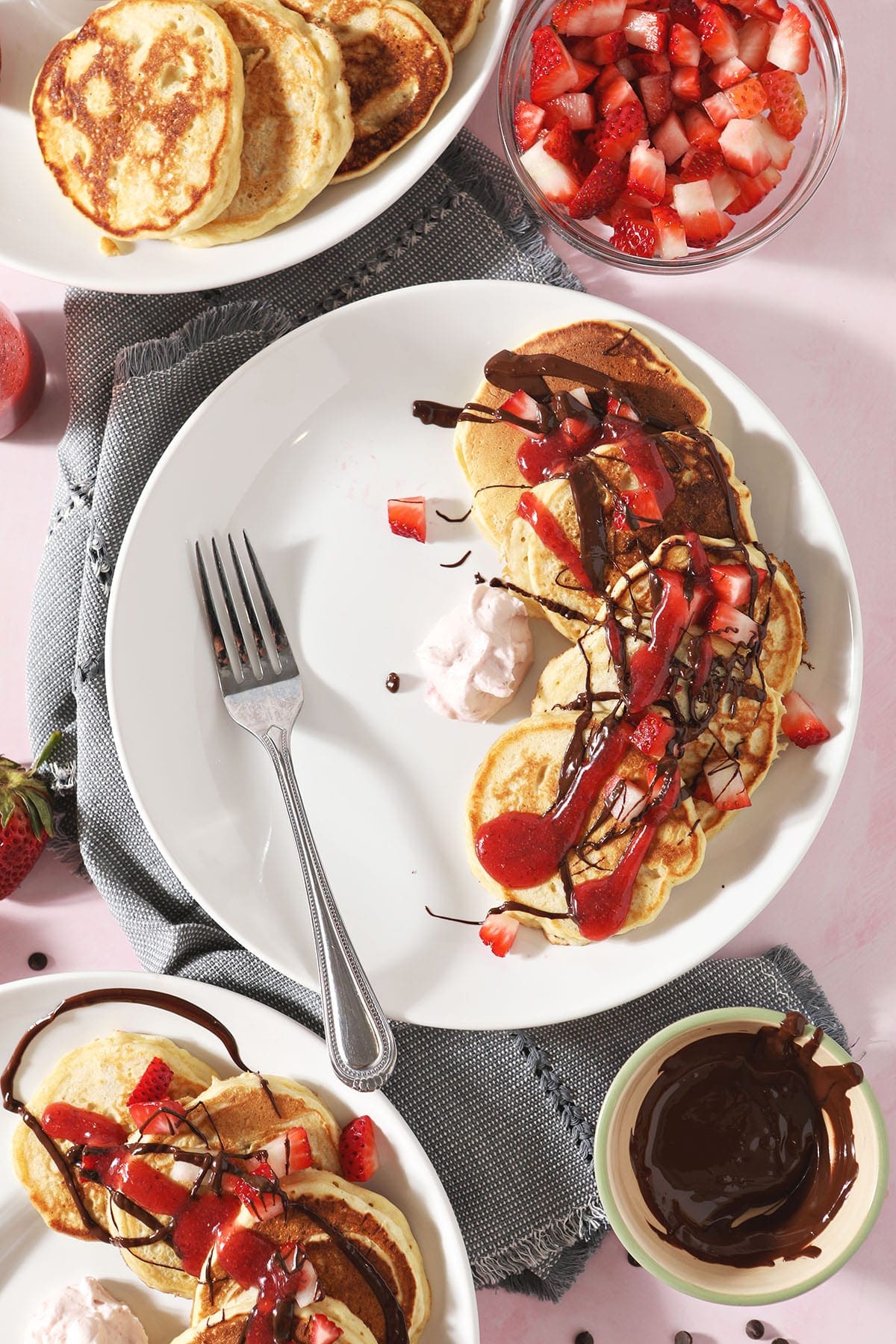 Three white plates holding Strawberry Pancakes with whipped cream, dark chocolate and strawberry sauce