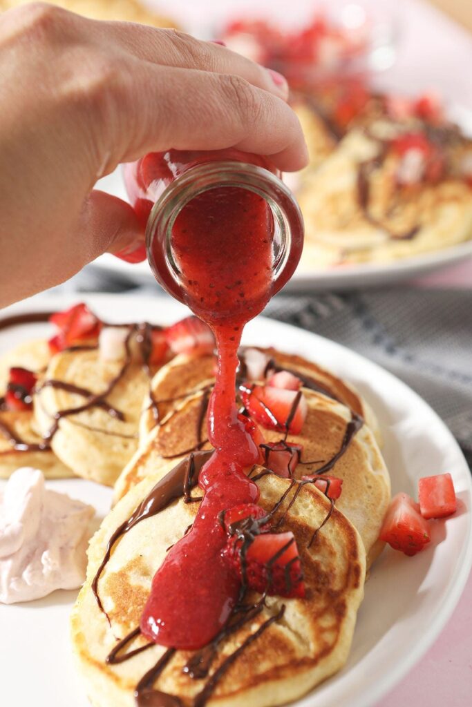 Strawberry sauce pours onto pancakes