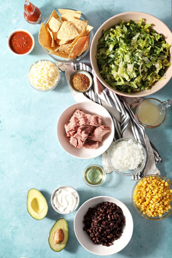 Ingredients to make taco salad with ground turkey in bowls on a turquoise countertop