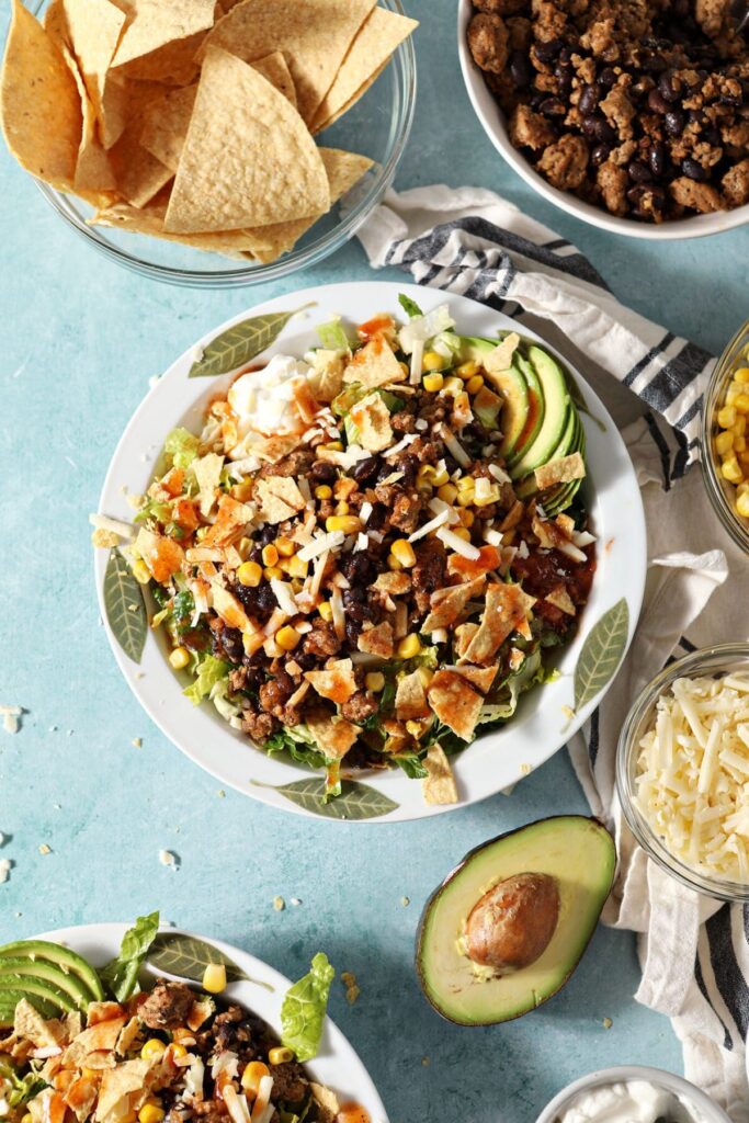 Two dressed turkey taco salads on a green countertop surrounded by ingredients