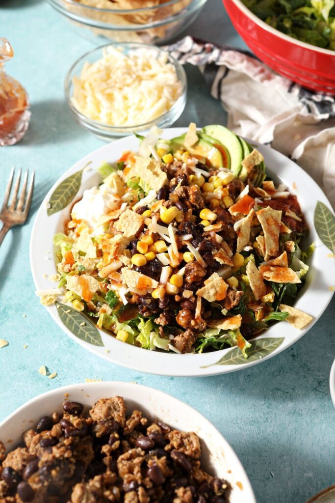 Two bowls of turkey taco salad on a green countertop next to bowls of toppings