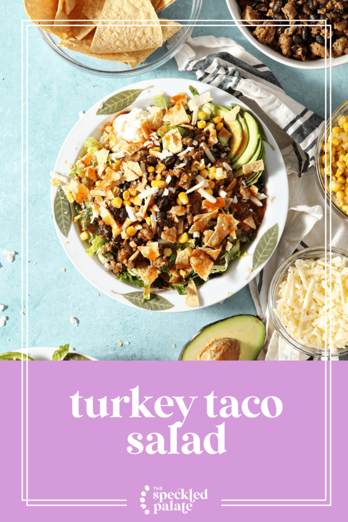 Two full taco salads in white bowls on a green countertop surrounded by ingredients with the text Turkey Taco Salad