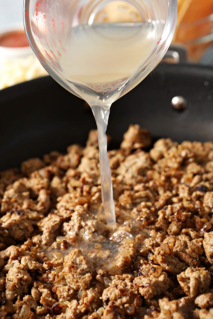 Chicken stock pours on top of ground turkey in a skillet