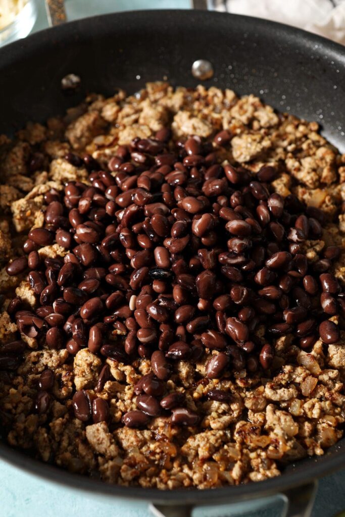 Black beans on top of cooked ground turkey in a skillet