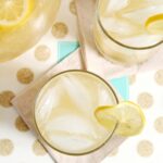 Overhead image of two glasses of lemonade next to a pitcher sitting on a gold and white polka dot platter on a blue tabletop