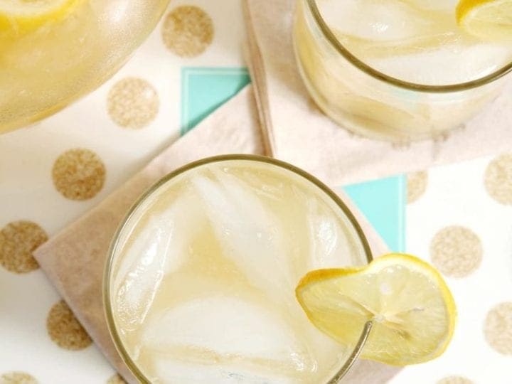 Overhead image of two glasses of lemonade next to a pitcher sitting on a gold and white polka dot platter on a blue tabletop