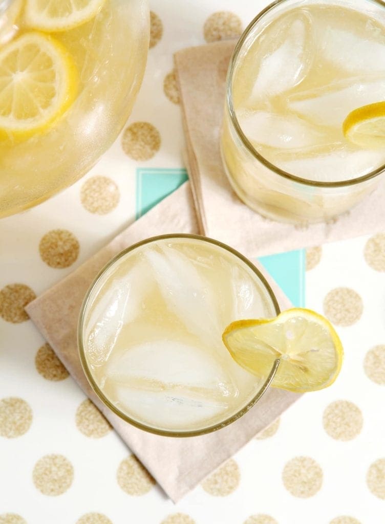 Overhead image of two glasses of lemonade next to a pitcher sitting on a gold and white polka dot platter on a blue tabletop