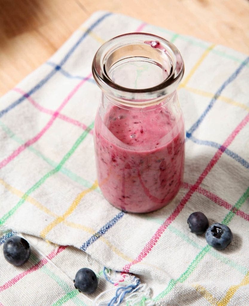 Homemade Blueberry Vinaigrette sits on a patterned kitchen towel with fresh blueberries, ready to be poured into the salad