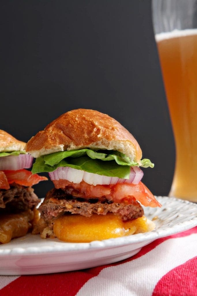 A Juicy Lucy Burger is cut in half with the cheese oozing out of it.