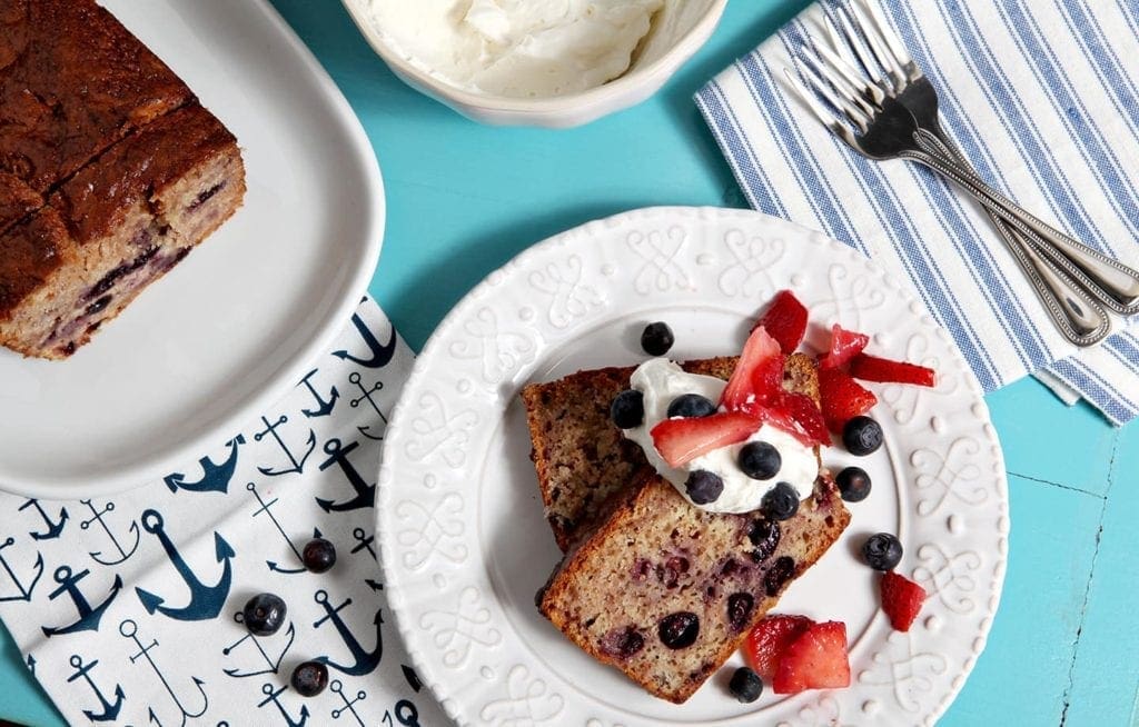 Two slices of berry pound cake are served with homemade whipped cream, blueberries and sliced strawberries