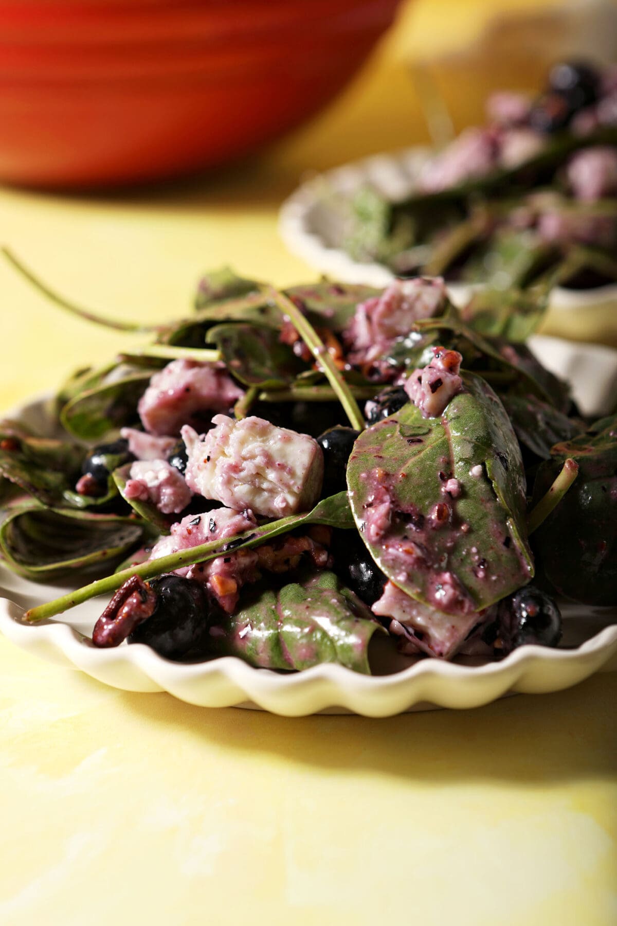 close up of Blueberry Salad with Feta, Chicken and Pecans on a scalloped white plate on a yellow surface