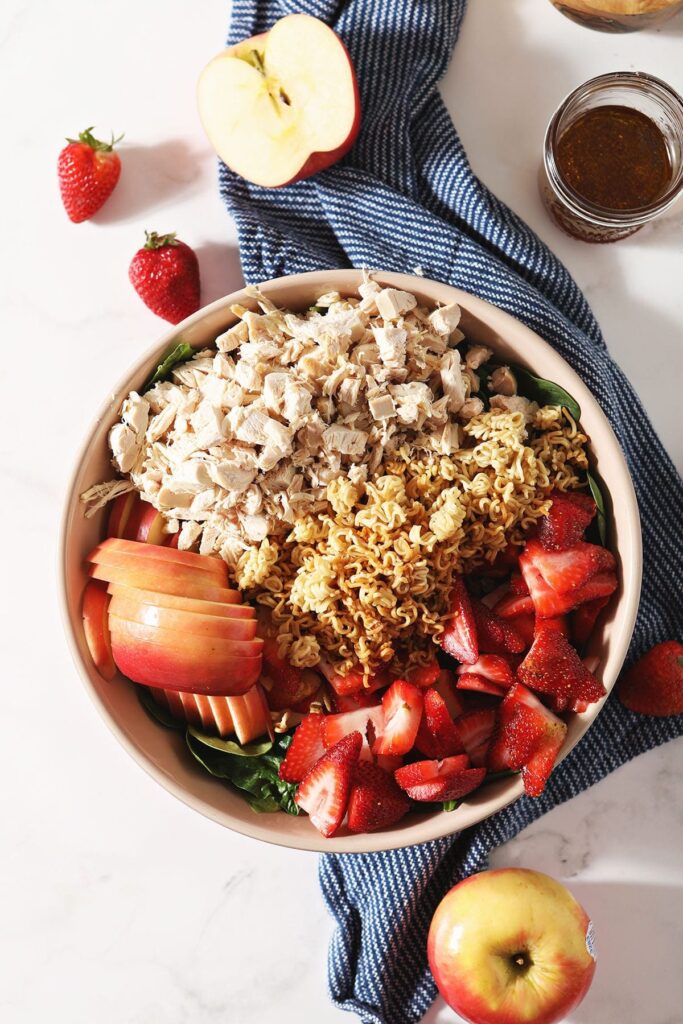 Chicken, ramen noodles and fruit on top of a spinach salad