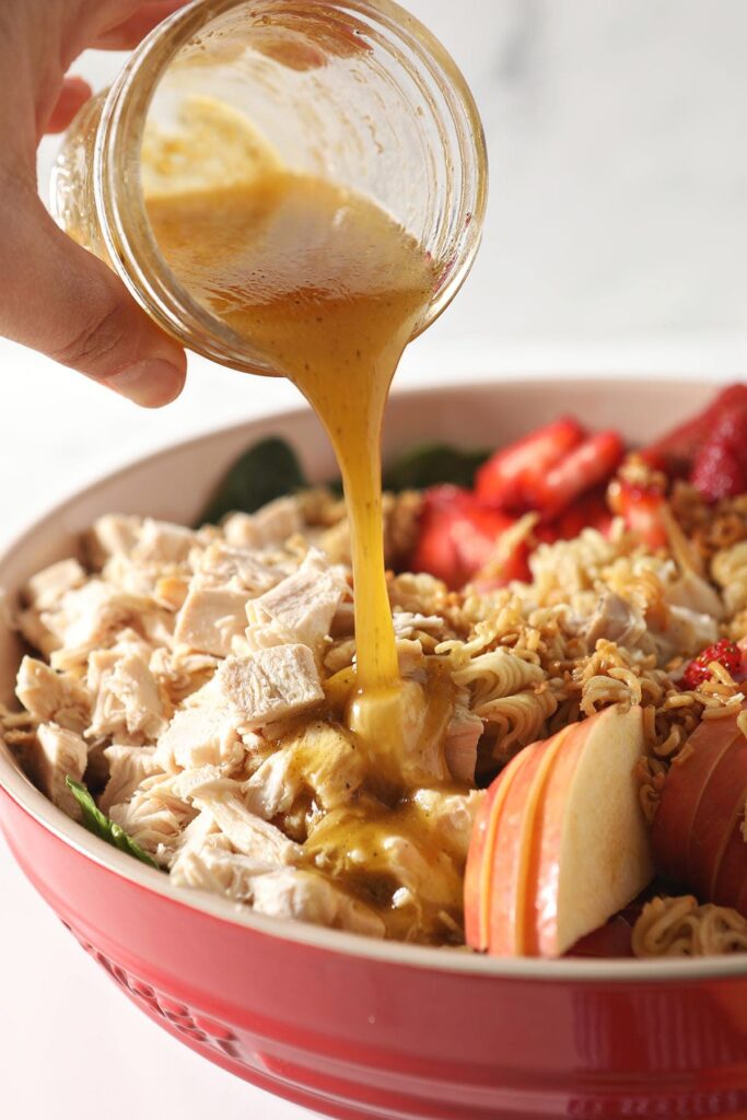 Honey vinaigrette pours on top of a chicken spinach salad with fruit