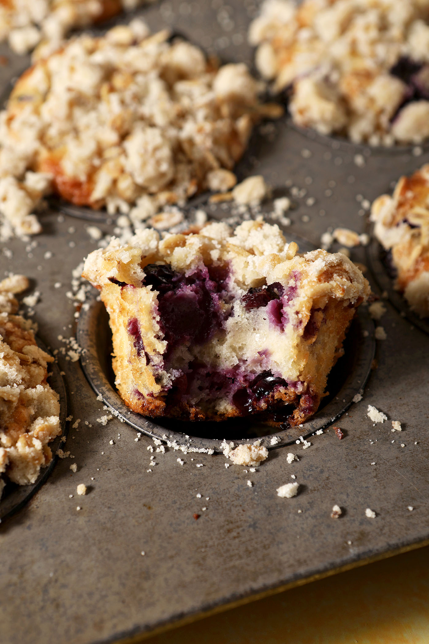 A bitten-into Lemon Blueberry Muffin in a muffin tin with more muffins