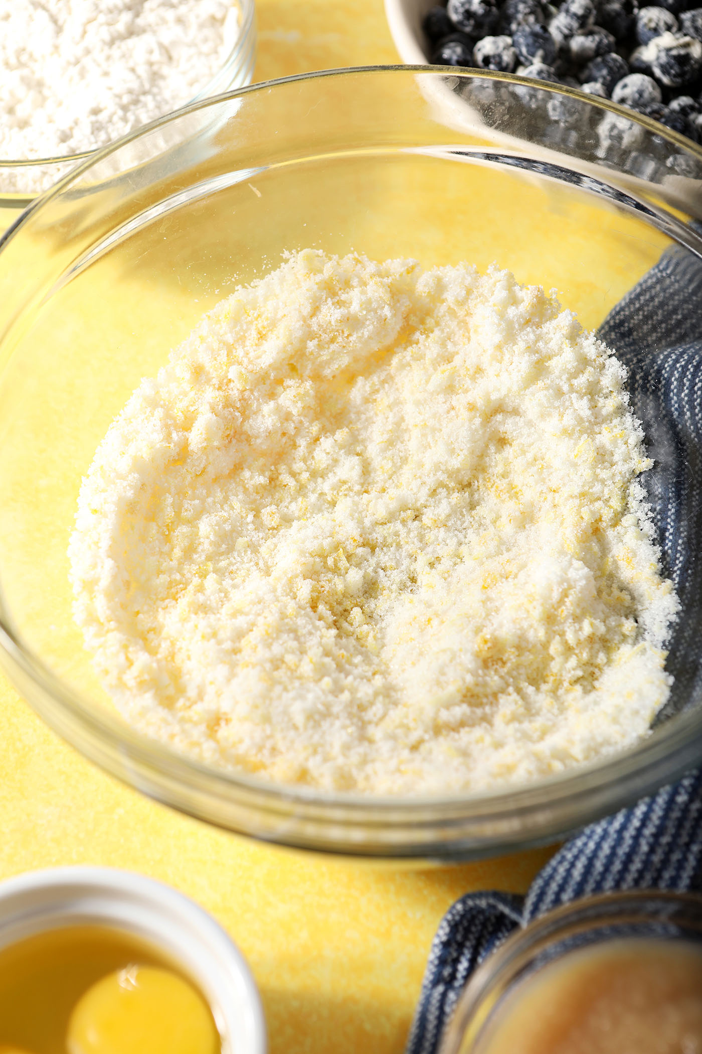 Lemon zest and sugar in a bowl on a yellow surface near a blue linen