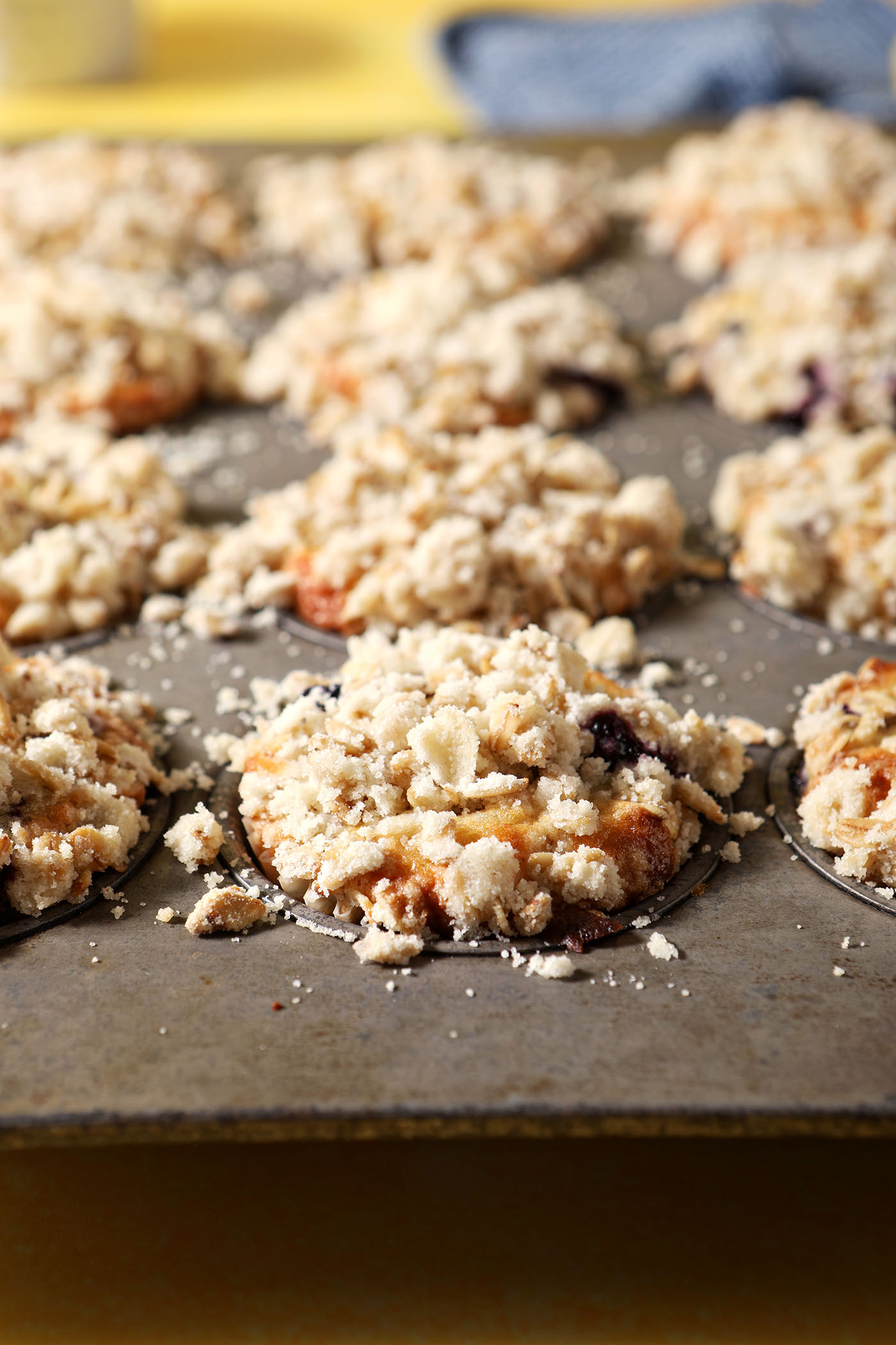 Baked Lemon Blueberry Muffins with Streusel Topping in a muffin tin on a yellow surface