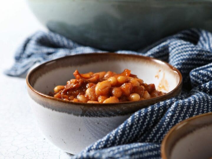 Two bowls of baked beans on a white tabletop with a blue striped towel
