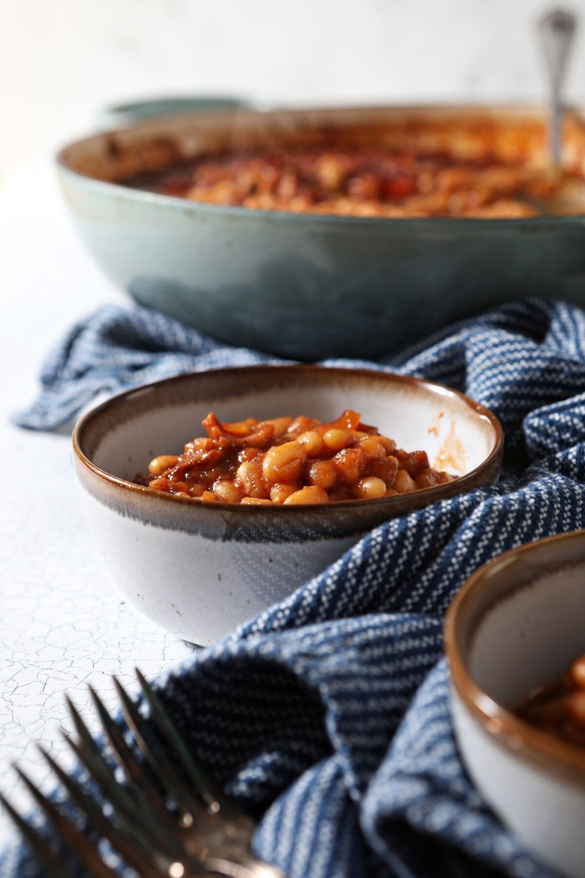 Two bowls of baked beans on a white tabletop with a blue striped towel