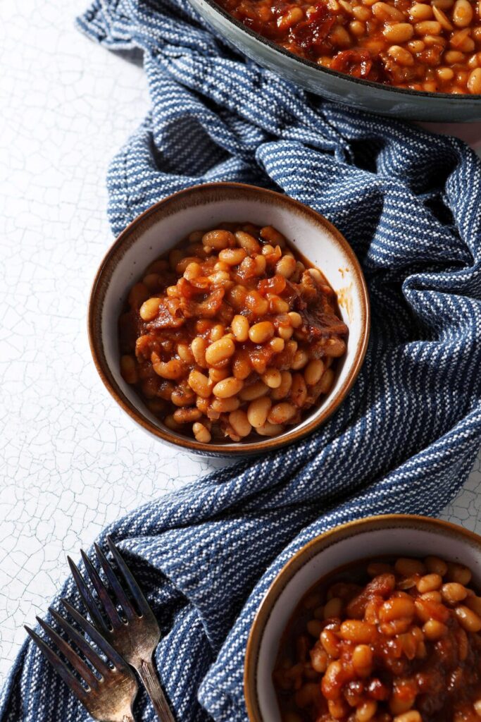 Three bowls of spicy baked beans from above with a blue striped towel