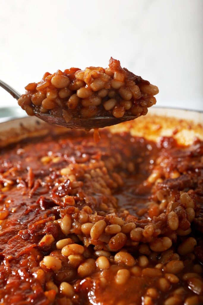 A spoon lifts baked beans out of a braiser pan