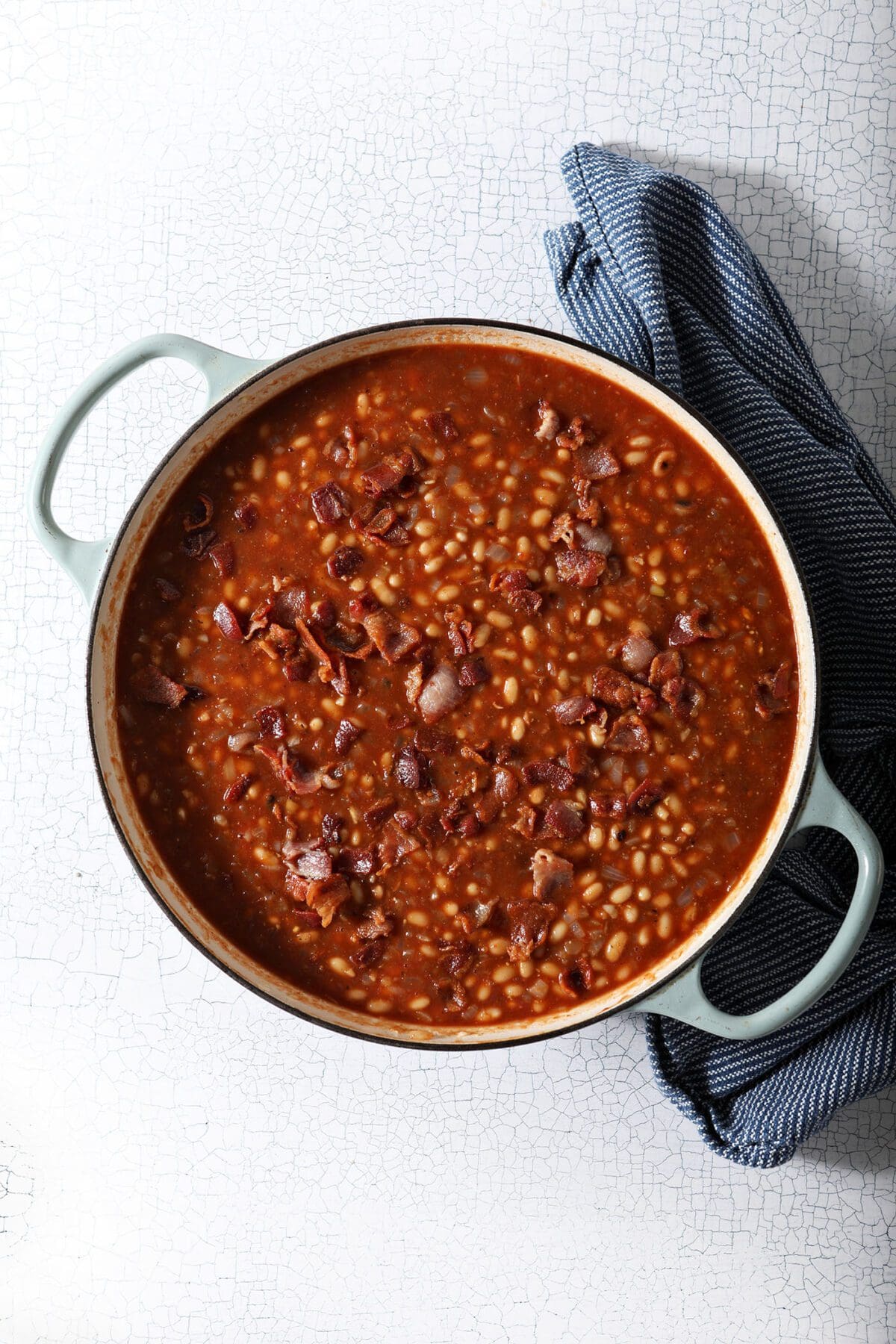 Overhead of baked beans in a pan before baking with bacon crumbles on top