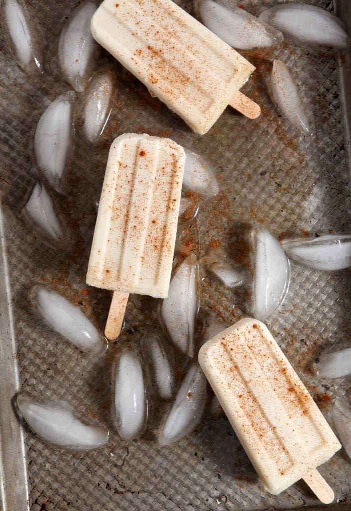 Several Vegan Spiced Rum Horchata Pops sit on a cookie sheet with ice cubes before serving