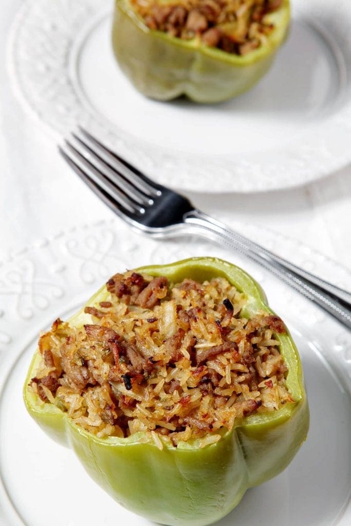 Cooked turkey jambalaya stuffed bell peppers on white plates with fork 